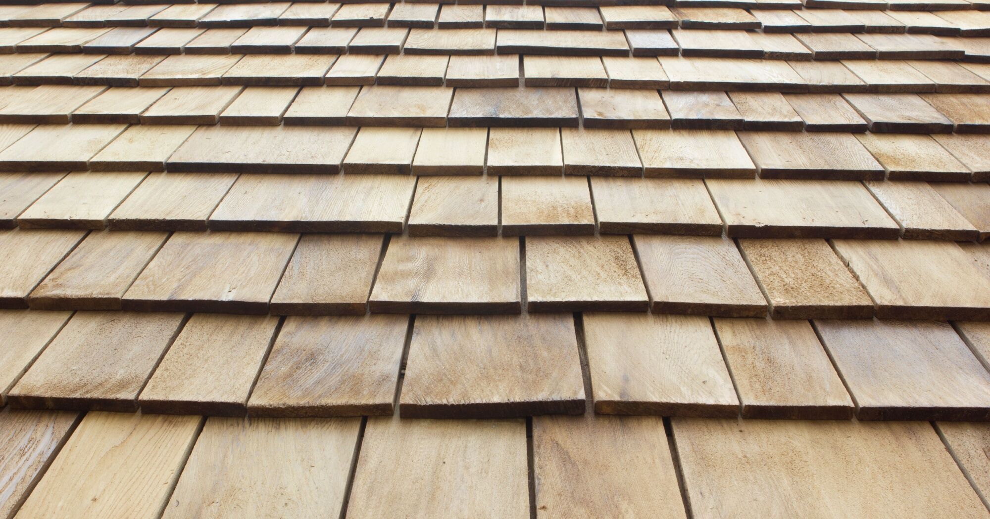 benefits-of-wood-roofing Close-up view of a wooden shingle roof, showcasing the natural texture, grain, and overlapping pattern of the wooden shingles.